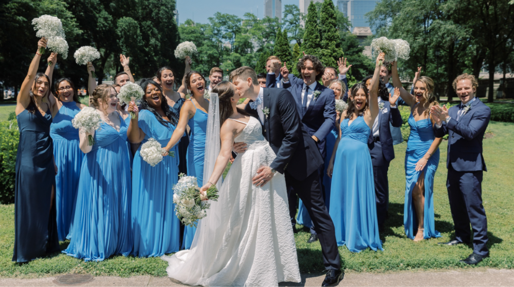 Alumni celebrate their wedding outside with their attendants in formal dress